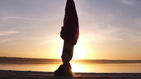 Close-up-footage-of-a-beautiful-girl-standing-stood-on-her-head-in-yoga-asana.-Sun-shines-and-water-on-the-background