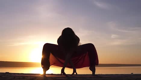 Silhouette-yoga-woman-practicing-Upaveshasana-on-sea-coast-at-beautiful-sunset.-Stunning-view-of-a-woman-in-yogi-pants.-Front-view