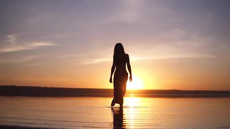 Front-footage-of-a-gorgeous-woman's-silhouette-step-on-a-water-in-the-morning-or-evening-dusk.-Slender-girl-in-a-yoga-pants