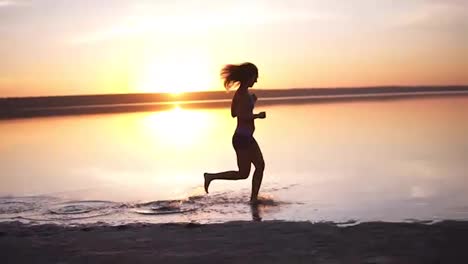 Silhouette-of-a-girl-running-on-the-water-on-a-sunset-or-sunrise-background.-The-slender-girl-runs-fast,-leaves-her-stains-on-the-water