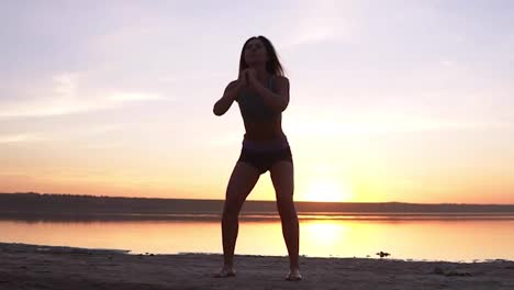 Young-attractive-woman-doing-sport-exercises-in-the-morning-on-sunrise-beach-by-sea-or-lake.-Doing-sit-ups-in-sportswear.-Healthy-lifestyle,-active-life,-work-out