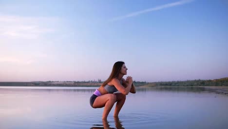 Side-view-of-young,-long-haired-woman-in-sportswear-doing-sit-ups-standing-in-the-water.-Happy,-healthy-lifestyle.-Beautiful-clear-blue-sky