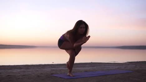 Beautiful-young-sporty-woman-wearing-sportswear-working-out-in-front-of-the-sea-or-lake,-doing-Eagle-Posture,-Garudasana,-full-length.-Dusk