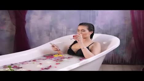 Beautiful-woman-relaxing-in-milk-bath-lying-in-bathtub-and-drinking-sparkling-wine,-using-smartphone-browsing-social-media-sharing-photos.-Shot-in-4k
