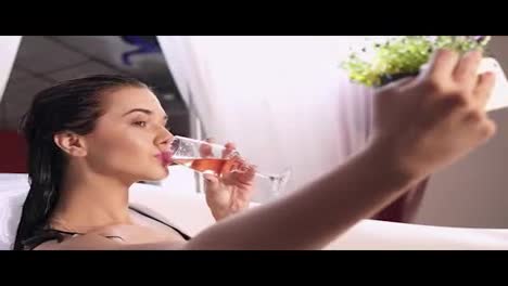 Beautiful-young-woman-taking-selfie-relaxing-in-milk-bath-and-drinking-sparkling-wine-from-a-glass.-Shot-in-4k