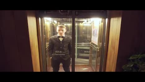Young-and-successful-businessman-in-a-suit-with-a-bow-tie-coming-out-of-the-Elevator-with-Glass-Doors.