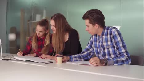 Group-of-young-people-on-the-meeting-in-modern-apartment.-Three-students-working-on-their-homework-sitting-together-at-the-table-and-drinking-coffee.-Slowmotion-shot