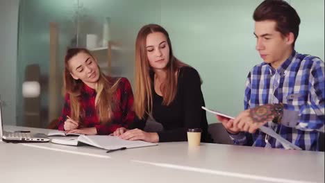 Three-students-working-on-their-homework-sitting-together-at-the-table-and-drinking-coffee.-Group-of-young-people-on-the-meeting-in-modern-apartment.-Slowmotion-shot