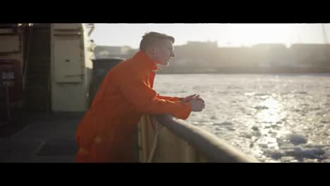 Young-man-in-orange-uniform-traveling-on-board-of-the-ship-in-winter.