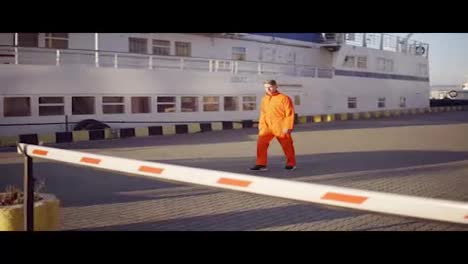 Dock-worker-in-orange-uniform-walking-in-the-harbor-through-the-barrier