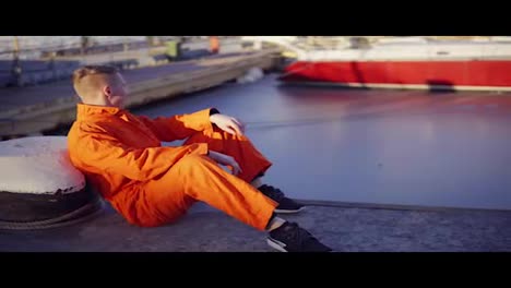Young-man-in-orange-uniform-sitting-during-his-break-by-the-sea-in-the-harbor