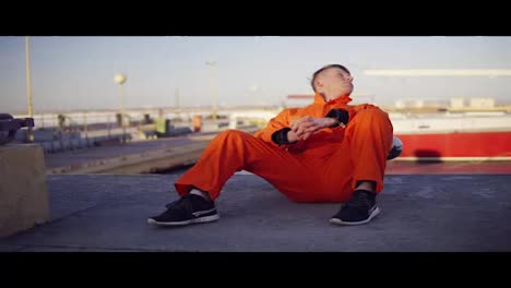 Young-man-in-orange-uniform-sitting-during-his-break-by-the-sea-in-the-harbor