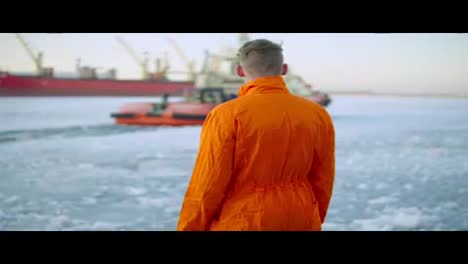 Dockarbeiter-In-Orangefarbener-Uniform-Mit-Blick-Auf-Das-Meer-Und-Im-Winter-Im-Hafen-Spazieren.-Vereistes-Meer