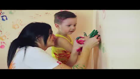 Happy-mother-and-her-cute-boy-having-fun-together-leaving-their-colorful-handprints-and-painting-on-the-wall.-Young-happy-family.-Mother-and-child-concept