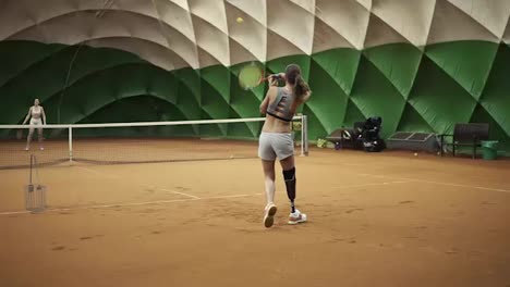 Two-beautiful,-tall-girls-in-sports-clothes-and-bras-are-playing-tennis.-Indoors.-Moving-camera
