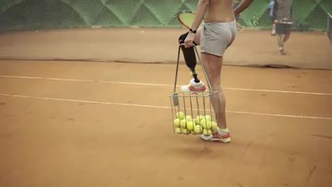 Close-up-footage-of-a-young-disabled-girl-picking-up-balls-from-a-tennis-court-and-with-racket-in-her-hand.-Short-shorts,-basket-for-tennis-balls.-Indoors