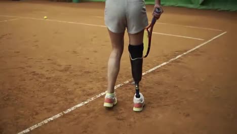 Attraktive,-Große-Behinderte-Frau-Spielt-Tennis,-Macht-Einen-Ballwurf.-Langhaarig,-In-Grauen-Shorts-Und-Sport-BH.-Drinnen
