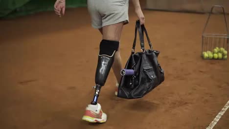 Attractive-injured-girl-with-a-sports-bag-in-her-hands-comes-to-the-indoor-tennis-court-to-train.-Making-first-ball-serve.-Slow-motion