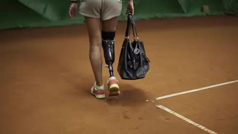 Tracking-footage-of-a-invalid-athlete-walking-on-the-tennis-court-with-the-racket-in-her-bag.-Back-view.-Slow-motion