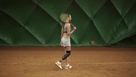 Disabled-young-woman-is-walking-through-the-tennis-court-with-racket.-Stands-in-the-stance.-Ready-for-match