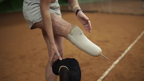 Injured-beautiful-brave-woman-athlete-puts-the-prosthesis-on-the-right-leg-standing-on-the-tennis-court.-Close-up
