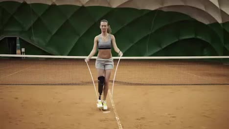 A-beautiful,-brave-girl-is-practicing-hard-with-a-skipping-rope-on-a-tennis-court.-On-the-right-foot-the-prosthesis-is-up-to-the-knee.-Front-view