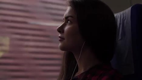 Pensive-girl-travels-by-train.-Sitting-next-to-the-window.-Looking-up.-Listen-music-in-earphones.-Thoughtful-look.-Side-view