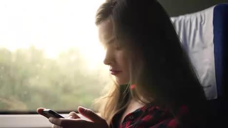 Close-up-footafe-of-a-long-haired-caucasian-girl-rides-on-a-train.-Sitting-and-chatting-in-mobile-phone.-Concentrated-andcalm.-Side-view