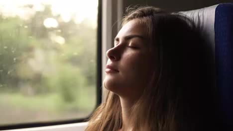 A-candid-female-traveling-by-train-and-falls-asleep-when-the-landscape-passes.-Beautiful-young-brunette.-Face-close-up