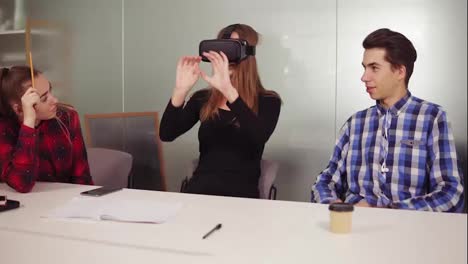 Eine-Hübsche-Frau-Probiert-Eine-App-Für-Eine-VR-Helm-Virtual-Reality-Brille-Aus,-Während-Ihre-Freunde-Und-Kollegen-Sie-In-Einem-Modernen-Büro-Unterstützen.-Team-Von-Arbeitern,-Die-Innovative-Zukunftstechnologie-über-VR-Headset-Nutzen