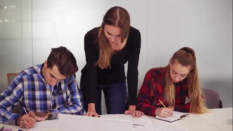 Three-students-working-on-their-homework-sitting-together-at-the-table-while-one-girl-is-dictating-and-two-other-students-are-writing.-Slowmotion-shot