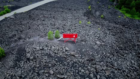 Large-red-bench-inserted-in-a-landscape-of-gray-volcanic-rocks-with-vegetation-of-a-few-green-plants
