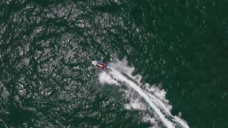 Extreme-jet-boat-roaring-across-the-sea-with-tourists,-Aerial-footage