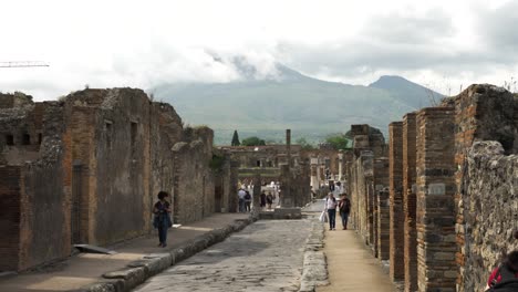 Ruinen-Von-Pompeji-Entlang-Der-Via-Della-Scuole-Mit-Dem-Wolkenverhangenen-Vesuv-Im-Hintergrund