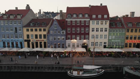 Experience-the-enchanting-sunset-over-Nyhavn,-Copenhagen,-where-people-gather,-and-boats-navigate-the-charming-canal