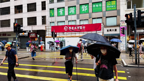 Einheimische-Aus-Hongkong-überqueren-Mit-Regenschirmen-Die-Straße-Bei-Leichtem-Regen
