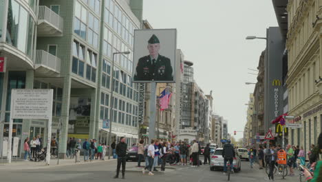 A-lively-street-scene-at-Checkpoint-Charlie-in-Berlin,-featuring-tourists-walking-around-the-historical-landmark