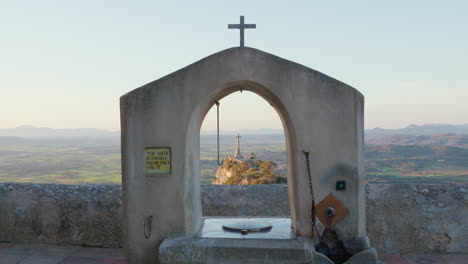 View-from-the-Monastery-of-San-Salvador,-Mallorca,-overlooking-a-hill-with-a-cross-and-mountains-in-the-background