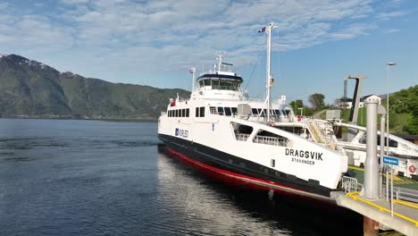 Electric-ferry-Dragsvik-from-Norled-company-alongside-ferry-pier-in-Sognefjord-Norway---Closeup-aerial-presenting-ship-laying-in-sea-with-blue-sky-summer-background