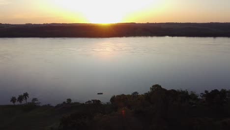 Cinematic-drone-footage-of-the-sunset-behind-trees-over-the-river-in-Misiones,-Jardin,-America,-Argentina,-Aerial