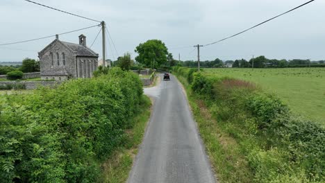Coches-Antiguos-Pasando-Una-Iglesia-En-Una-Carretera-Rural-Carlow-Irlanda-En-Un-Rally-De-Coches-Antiguos-En-Un-Cálido-Día-De-Verano