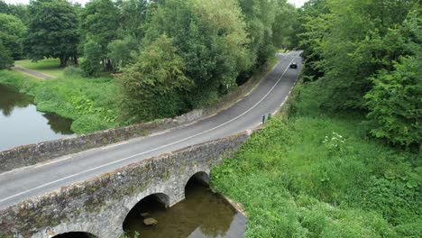 Vintage-car-driving-over-ancient-bridge-at-Kilkea-Co-Kildare-Ireland-on-a-vintage-motor-rally-on-a-warm-July-Day