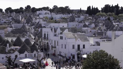 Panoramic-view-of-Alberobello's-village-and-many-tourists-walking-aorund-on-a-sunny-summer-day