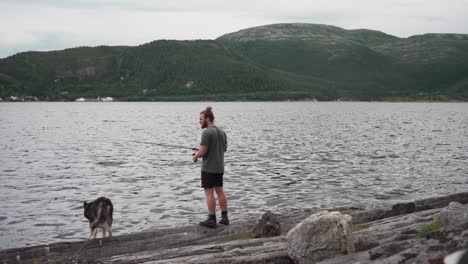 Un-Hombre-Pescando-En-Un-Lago-Con-Su-Perro-Mascota-Durante-El-Día-Nublado