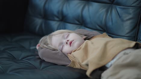 Witness-the-restful-nap-of-a-3-year-old-Caucasian-boy-in-a-medium-shot,-as-he-sleeps-serenely-on-a-black-leather-couch