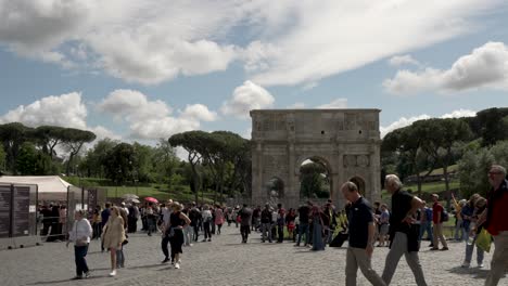 Una-Toma-En-Cámara-Lenta-De-Turistas-Disfrutando-De-Un-Día-De-Turismo-Bajo-El-Sol-Con-El-Arco-De-Constantino-Al-Fondo,-Roma,-Italia