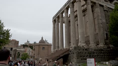 Establishing-shot-of-the-entrance-to-the-beautiful-Temple-of-Antoninus-and-Faustina,-tilting-down-to-reveal-the-crowds-of-tourist-who-are-visiting-the-famous-landmark,-Rome,-Italy