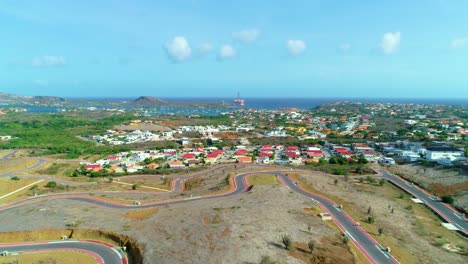4k-drone-reveal-of-houses-and-neighborhoods-near-the-Caribbean-sea-on-Curacao,-oil-drilling-platform-docked-in-distance