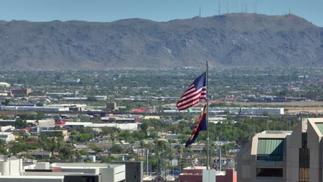 American-flag-and-Arizona-state-flag-waving-in-front-of-sprawling-city-suburbs-and-large-mountain-landscape