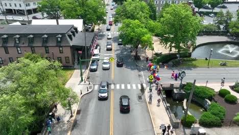 Drone-view-of-a-main-street-bustling-with-traffic-and-people-with-pride-umbrellas-gathering-near-a-park-for-a-pride-festival-on-a-summer-day